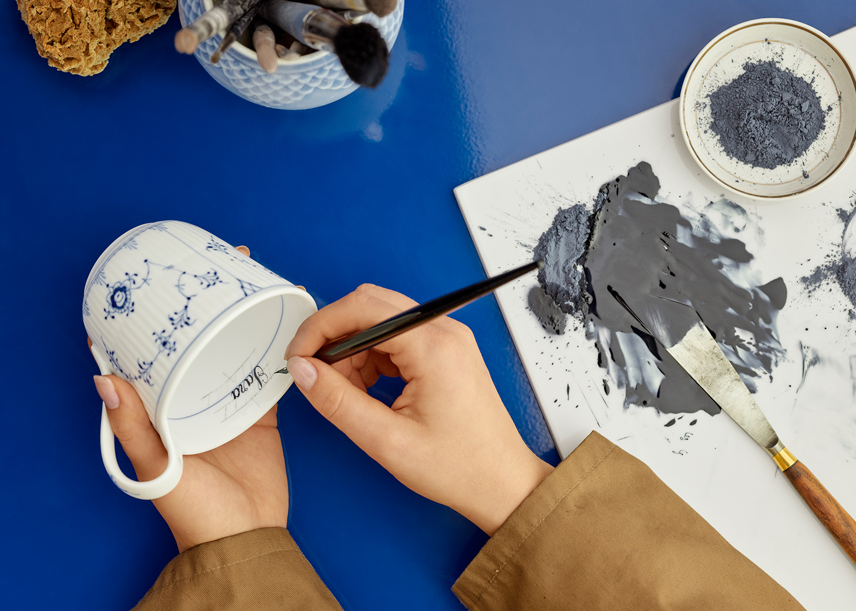 A Blue Fluted Plain High Handle Mug 33 cl being painted with a name on the inside of the cup
